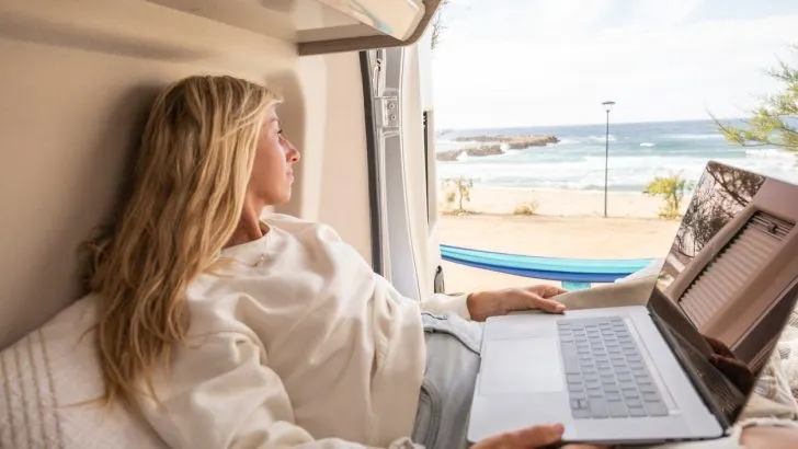 View of woman working on her laptop from a wild camping spot, Sardinia, Italy.