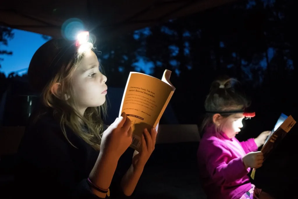 Two little girls reading books while camping with  headlamps