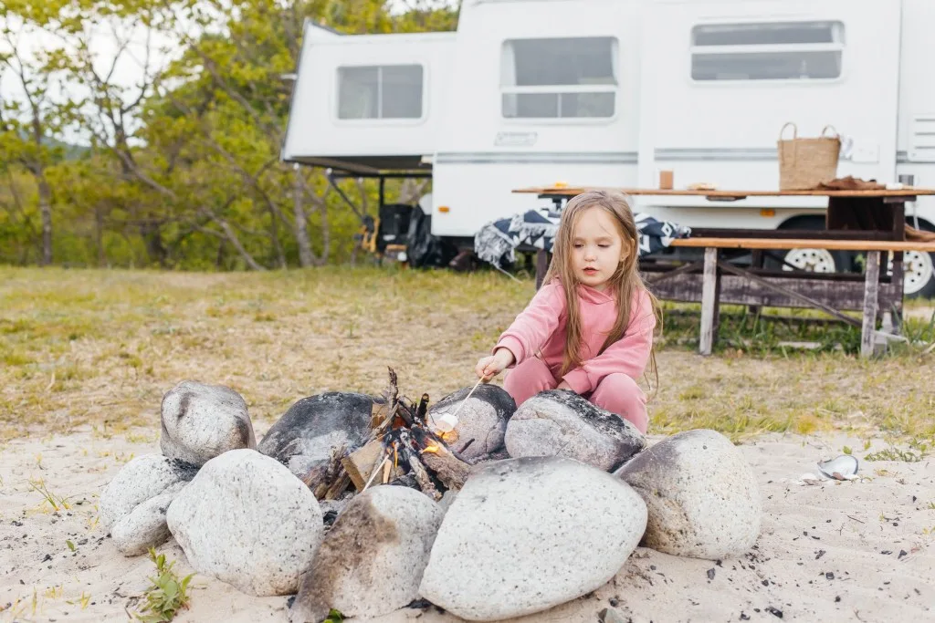 Little girl roasting marshmallow over campfire in front of RV