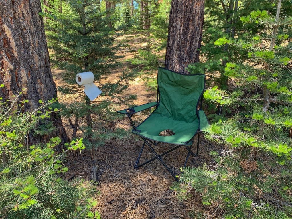 Camping chair with hole and toilet paper hanging in tree