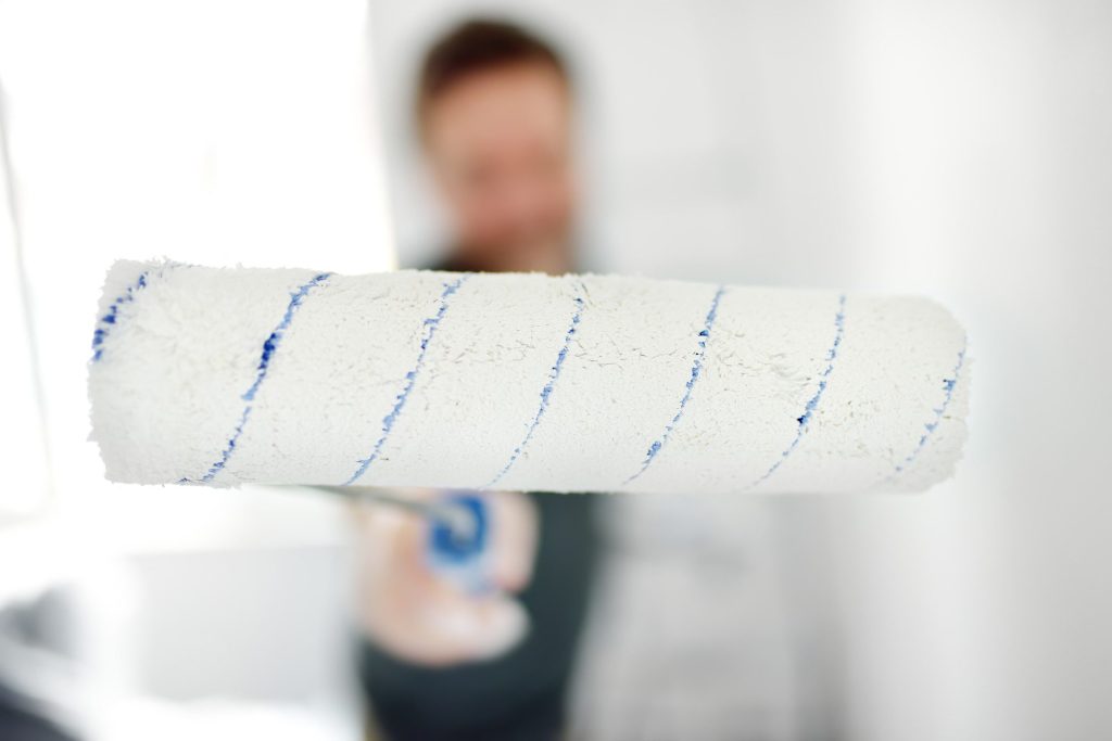Man holding clean paint roller at the camera.