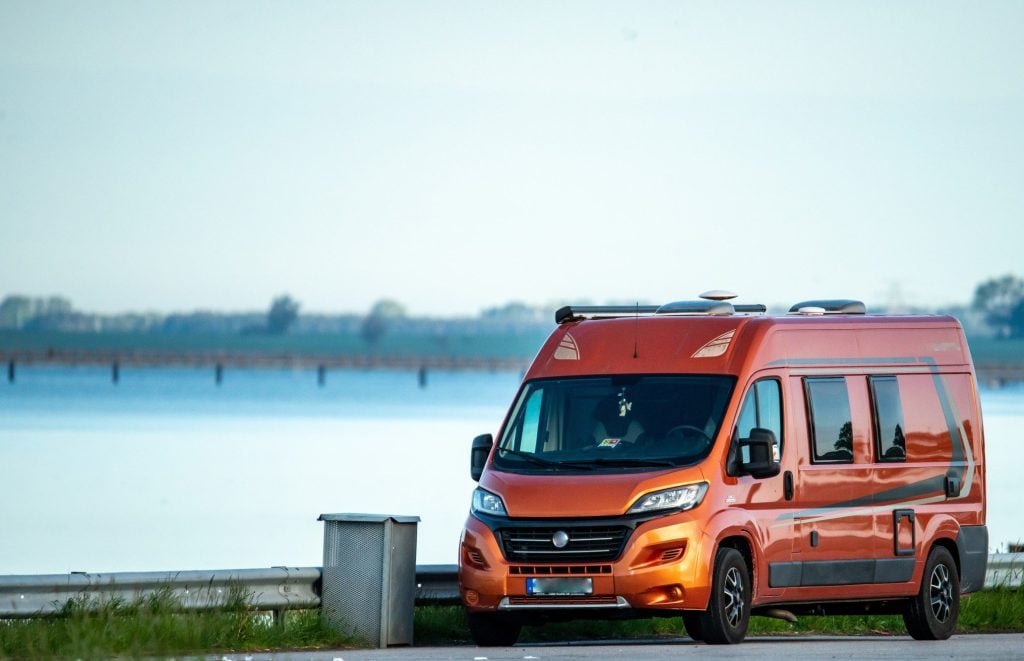 Orange camper van driving next to lake