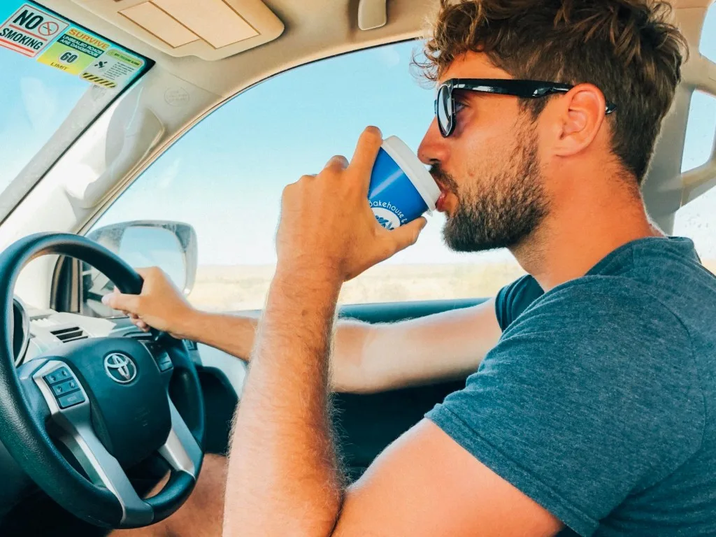 Man drinking coffee while driving on a road trip