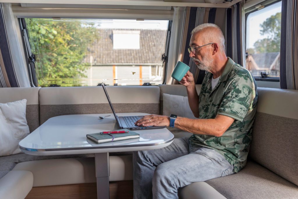 Man drinking cup of coffee inside RV while planning trip on laptop