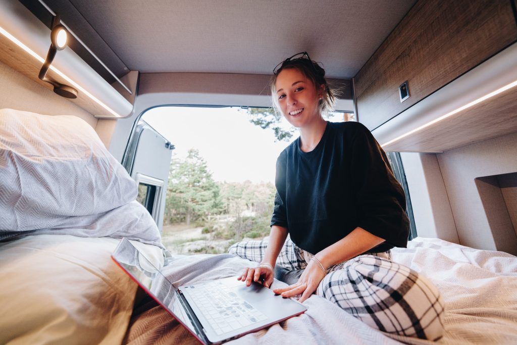 Woman on laptop sitting in bed in RV parked along the side of the road.