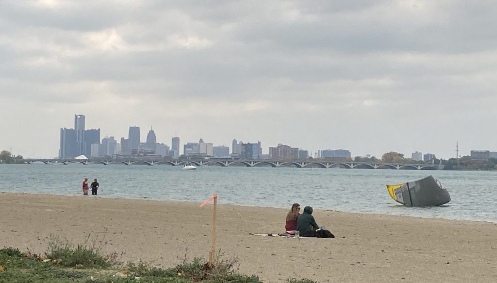 Couple sitting together on Belle Isle Beach with Detroit Skyline in the background.