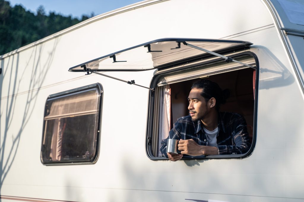 Man drinking coffee while looking out window of RV after sleeping in a public park