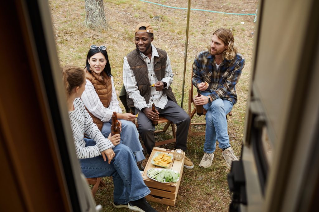 Group of four friends eating food in front of RV while camping