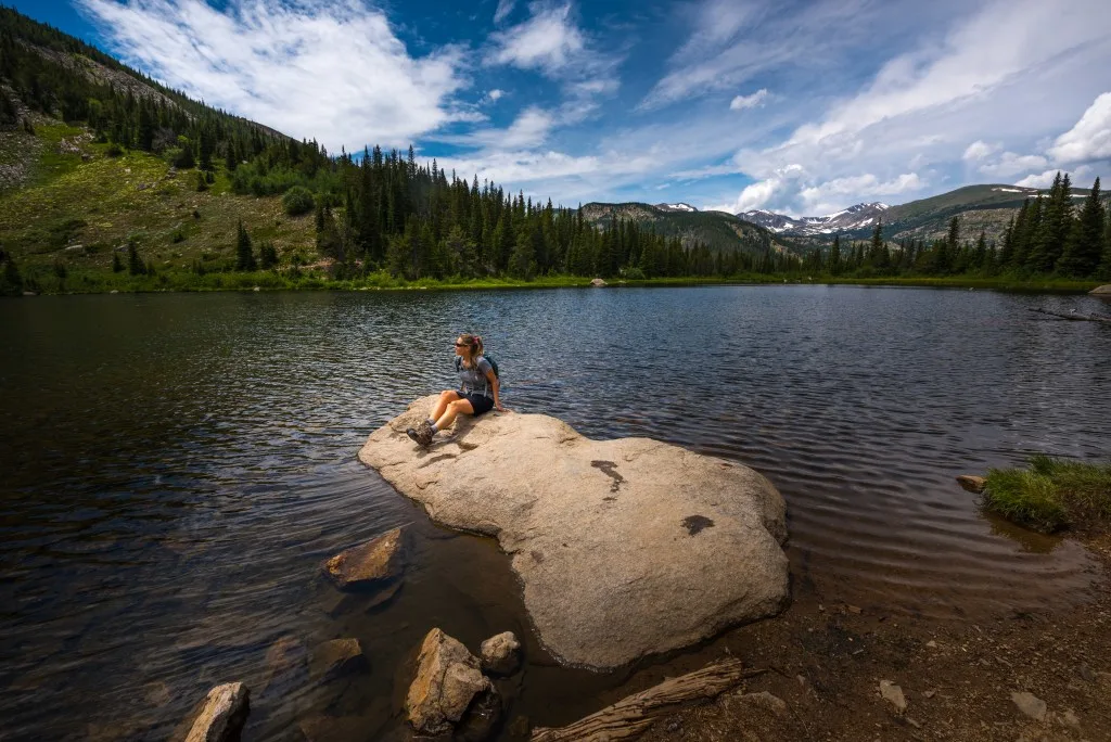 Woman sitting on rick in lake while hiking in Colorado
