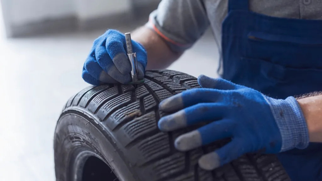 Mechanic checking tire tread depth and wear using a tire gauge, car maintenance concept