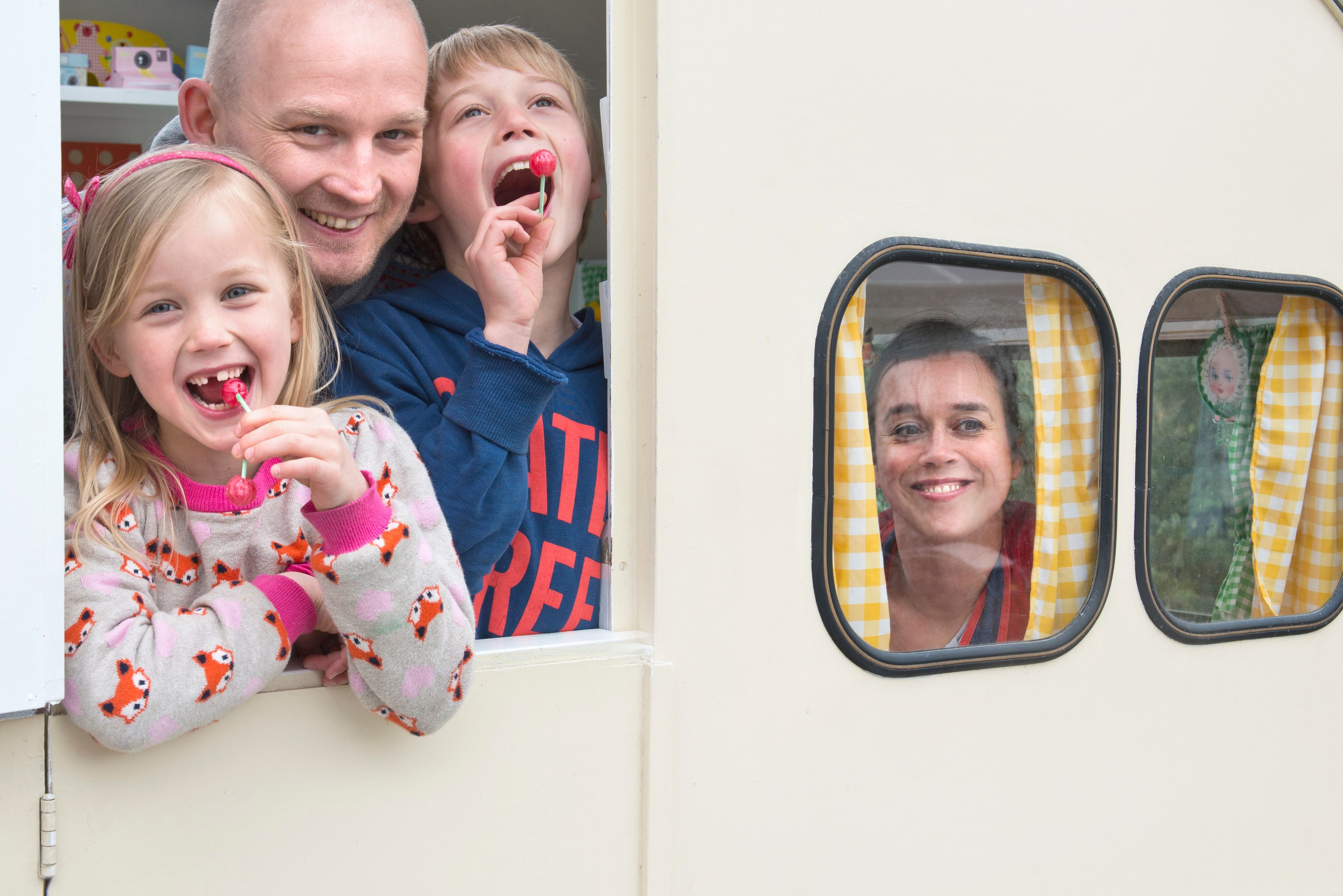 Family of four smiling out RV windows