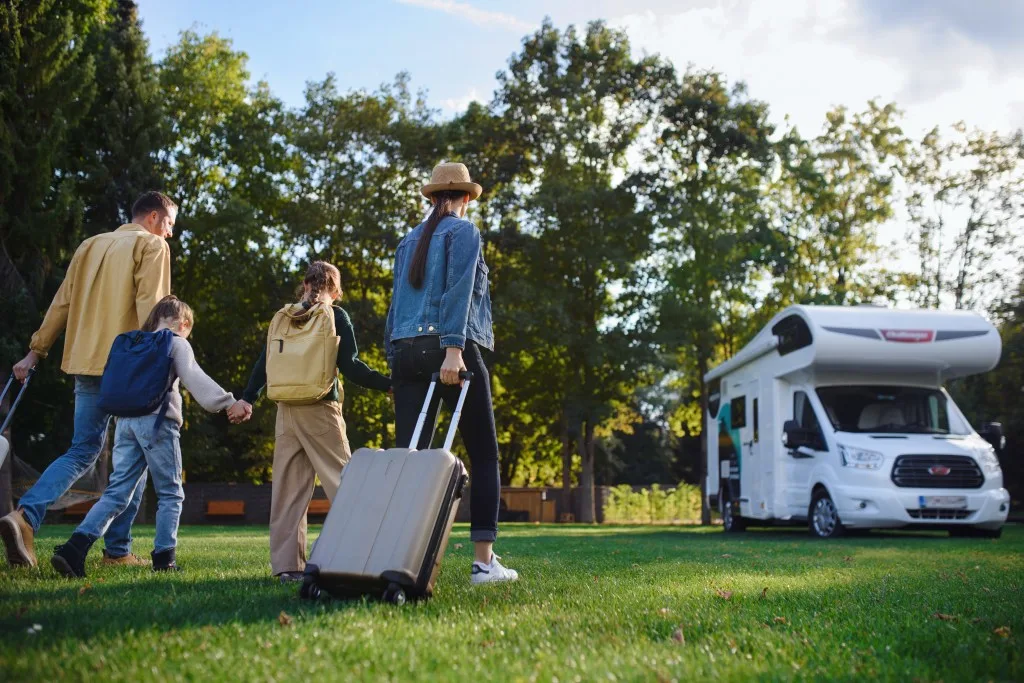 Family rolling suitcases to RV while camping in a public park for the evening