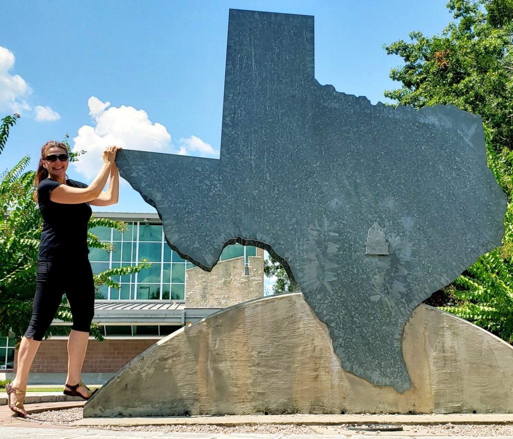 Woman visiting Texas posing next to sculpture of the state