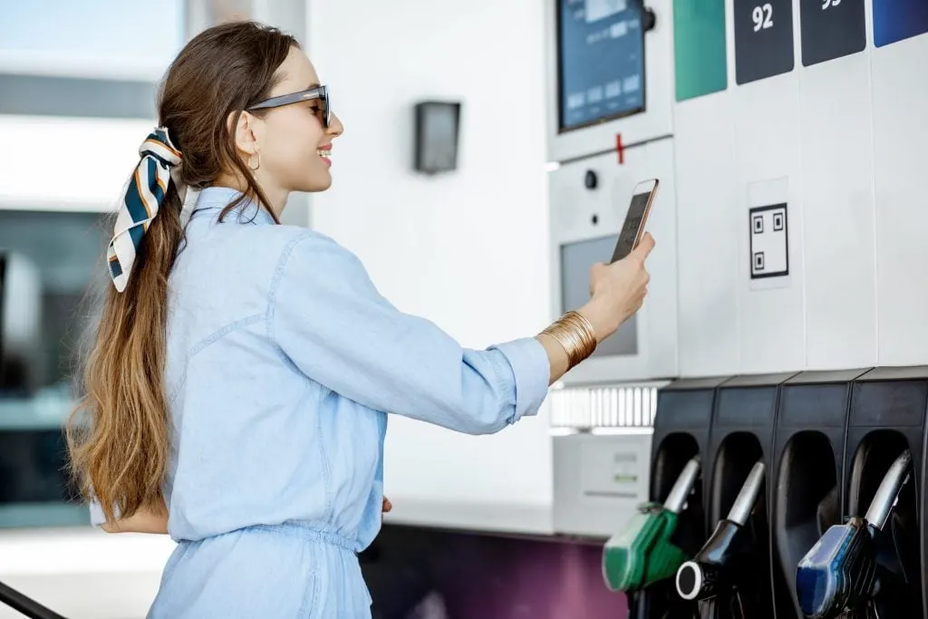 Woman paying with phone for gasoline, photographing bar code on the gas station pump