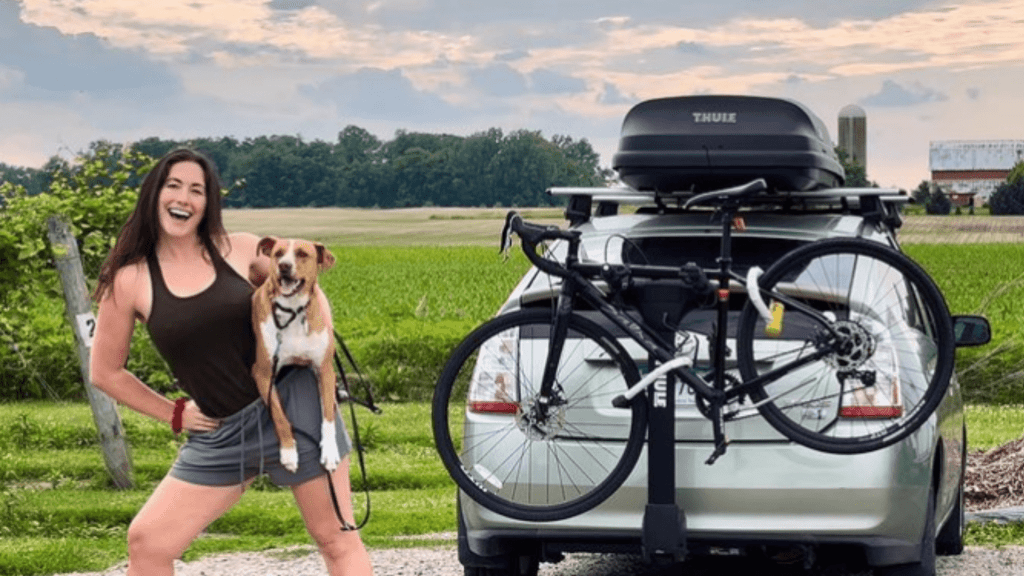 Nikki Delventhal and dog Camper smiling in front of her Prius.