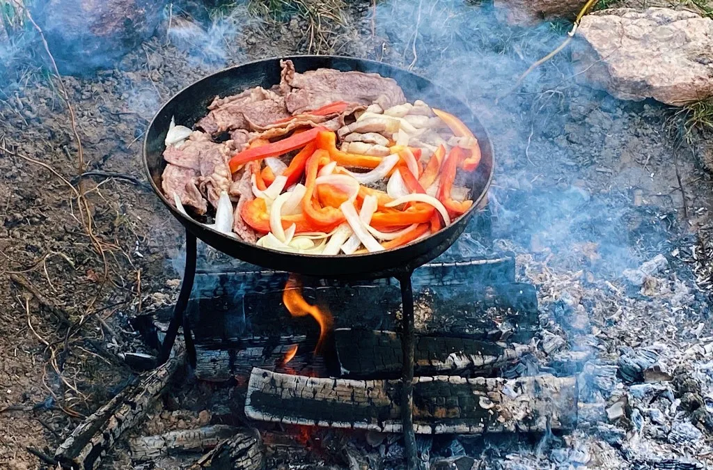 Meat and veggies cooking in campfire cooking kit over campfire