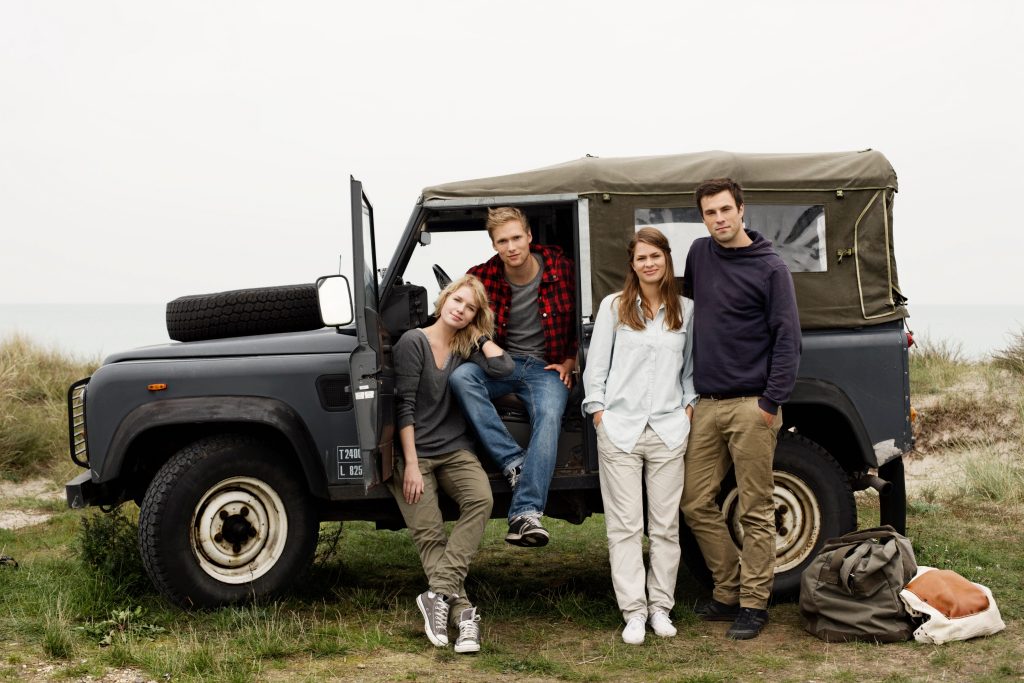 Group of four friends standing in front of Jeep while on a road trip. 