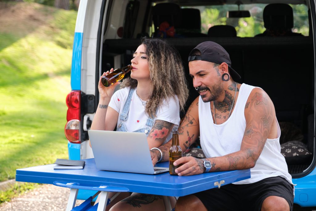 Young tattooed couple , drinking beer and using a laptop while in camper van
