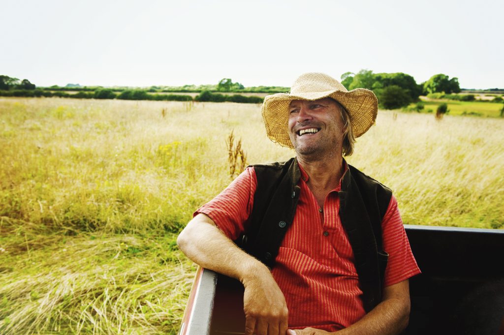 Man sitting in the back of a truck driving through a field.