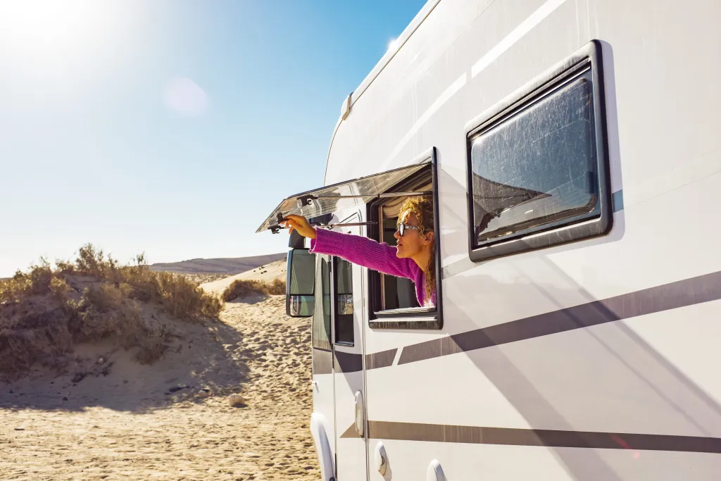 Woman looking out RV window on the beach in California. 