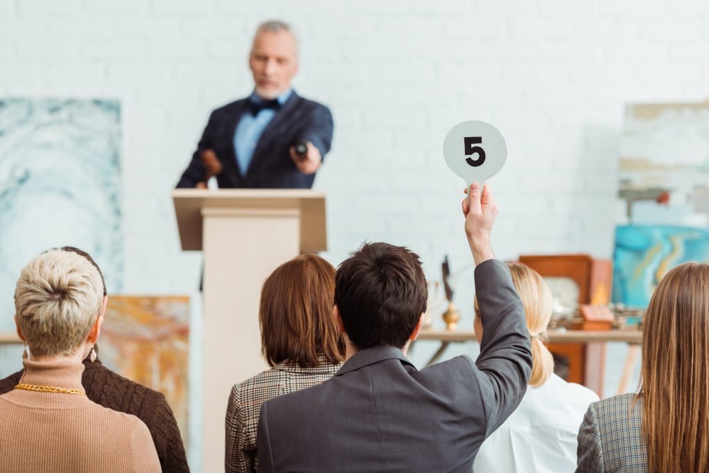 Back view of buyer showing auction paddle with number five to auctioneer during auction