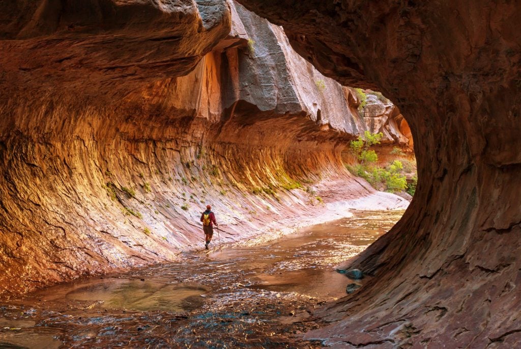 Person hiking  through shallow water in cave in Zion National Park