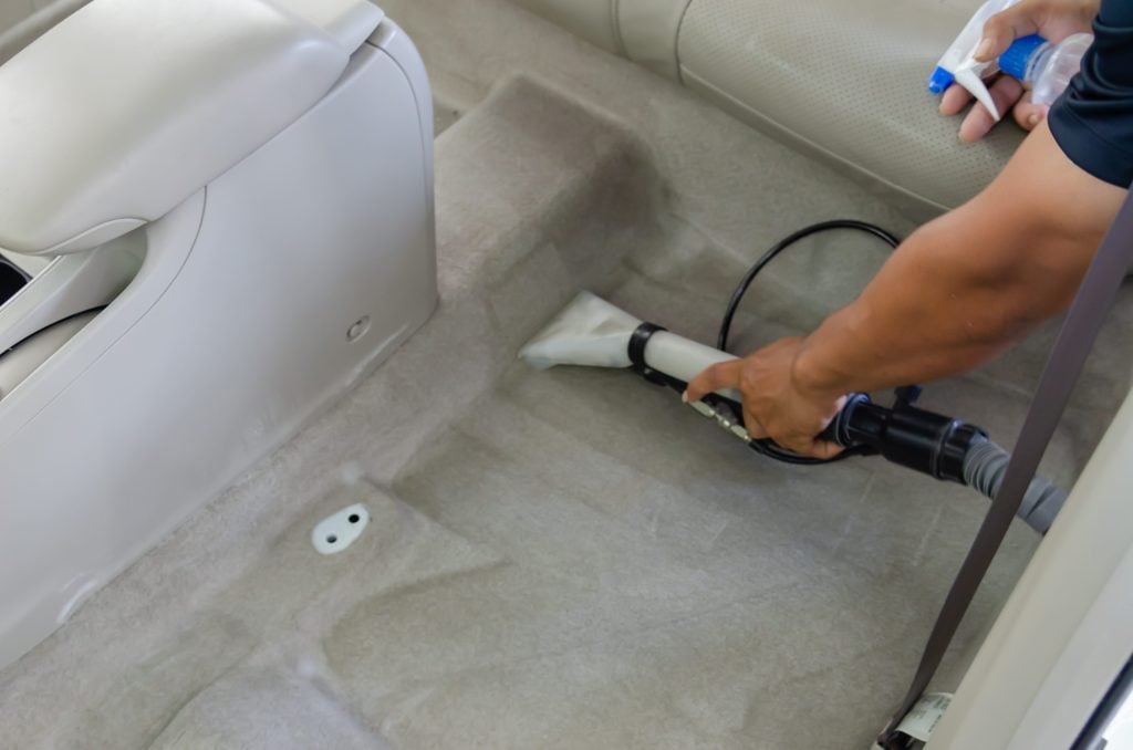 Man vacuuming car rugs while detailing the interior.