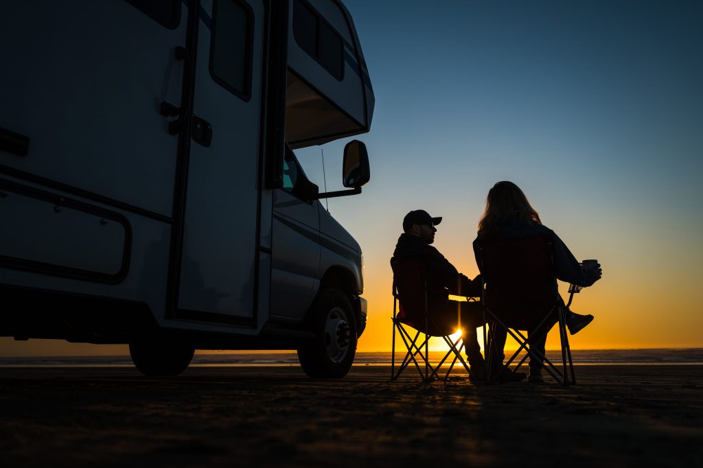 Couple sitting on beach next to RV at sunset