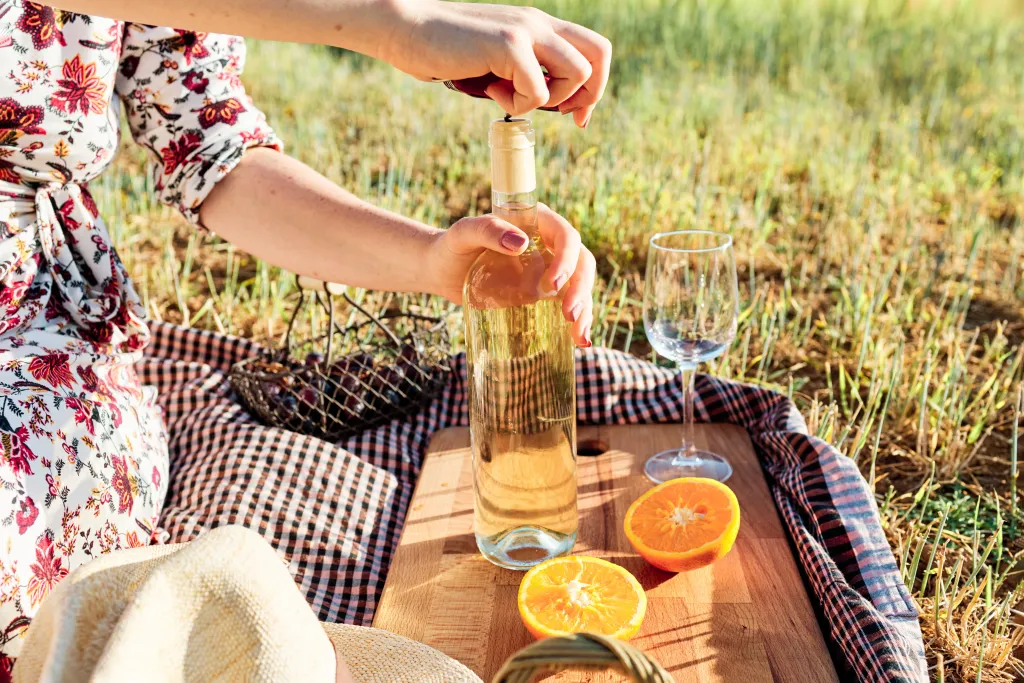 Woman opening a bottle of wine without a corkscrew on a picnic