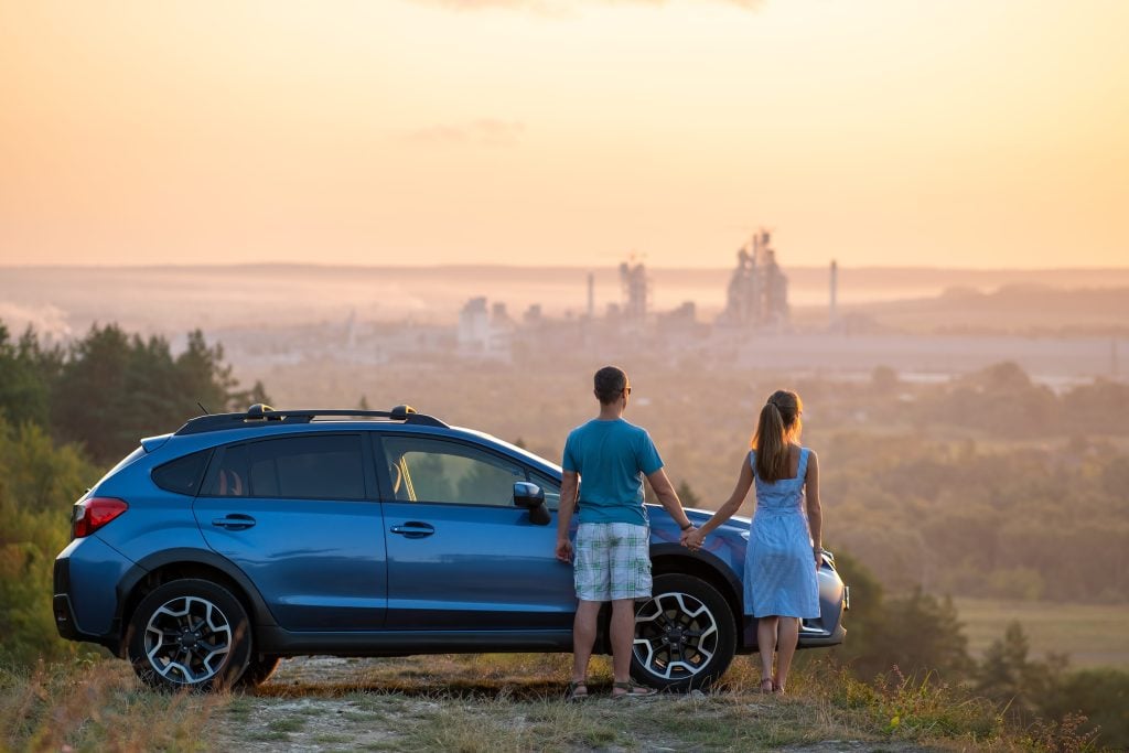 Couple holding hands in front of Subaru Outback at sunset