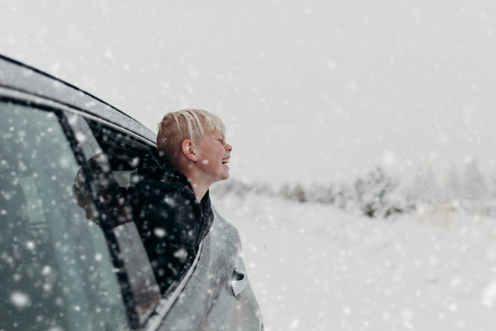 Boy leaning out car window while it is snowing.