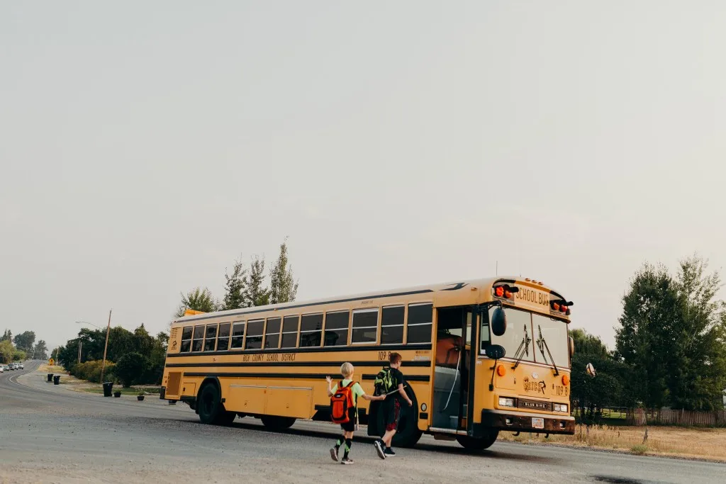 Two kids getting on school bus in the morning