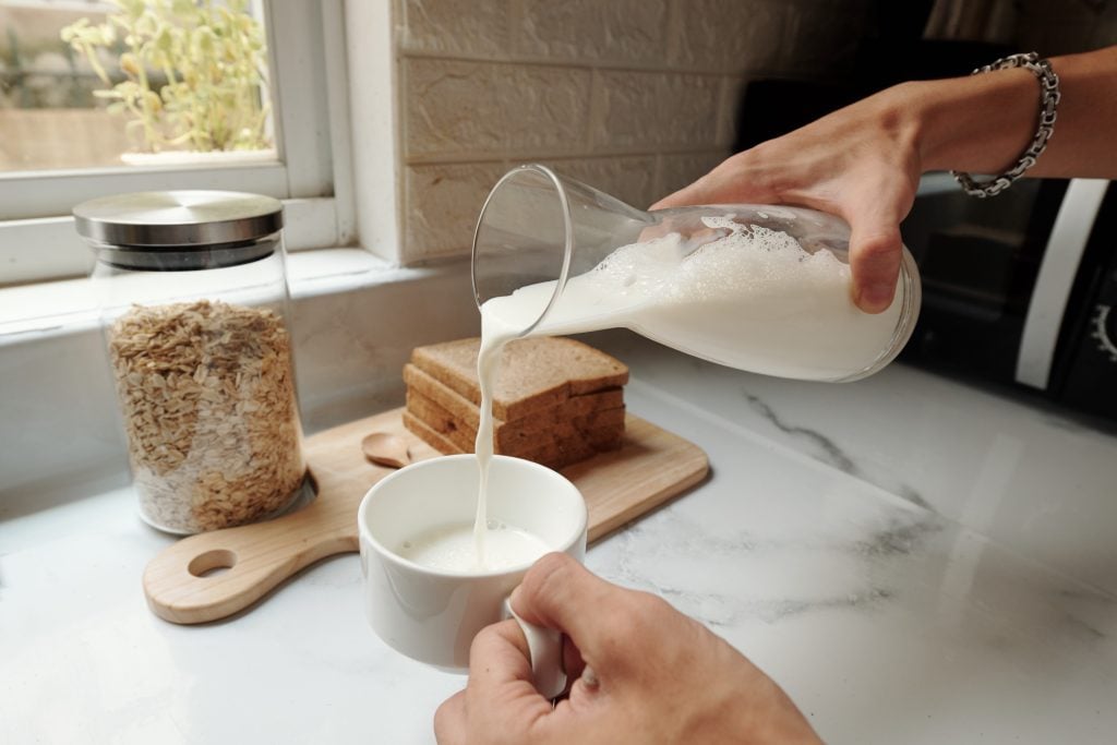 Hands pouring nut milk into measuring cup as a substitution for evaporated milk.