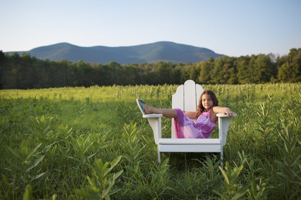 Little girl sitting on Adirondack chair in open field