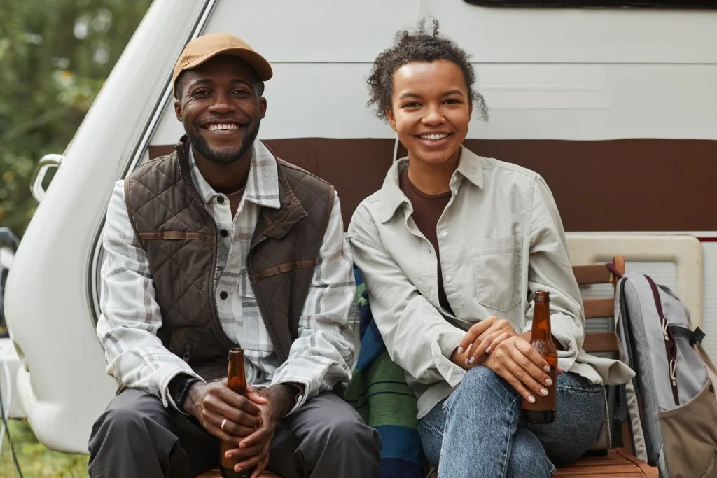 Couple sitting in front of RV together drinking beer