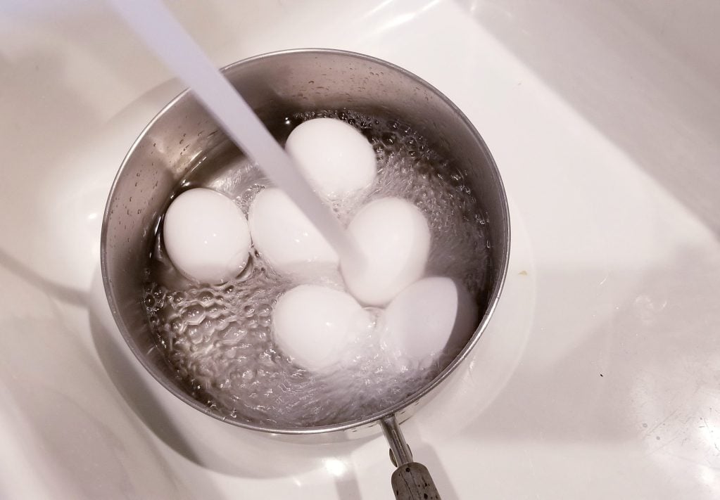 Eggs in pot with water pouring in to hard boil
