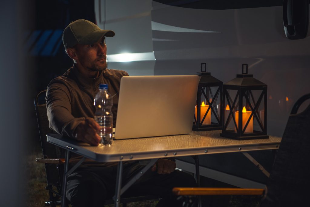 Man using laptop at night while sitting in front of RV