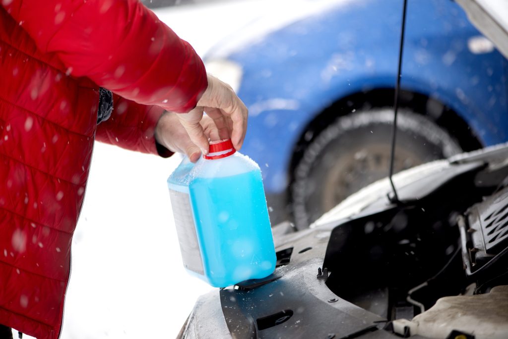 Person pouring antifreeze into vehicle in the snow