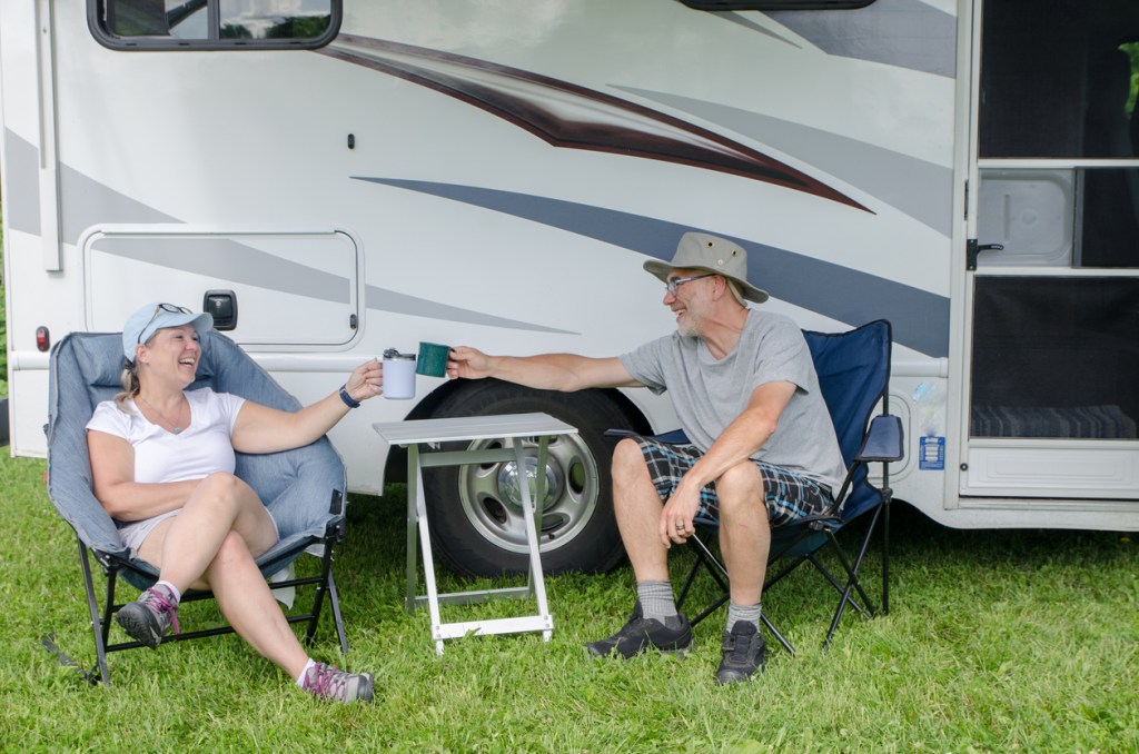 A couple clinking mugs as they relax in front of their RV after doing the hookup process