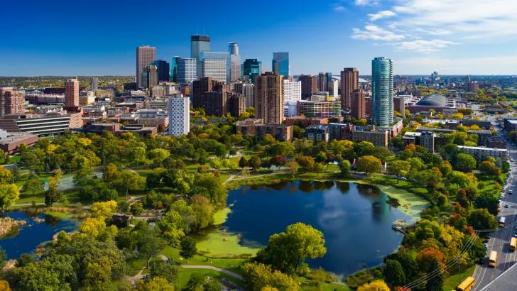 A photo of the Minneapolis skyline behind a lush green park and small lake