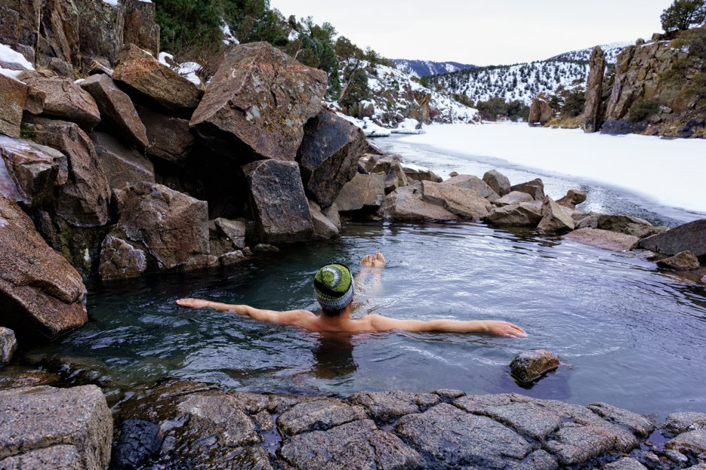 A man soaking in a hot spring that's surrounded by snow