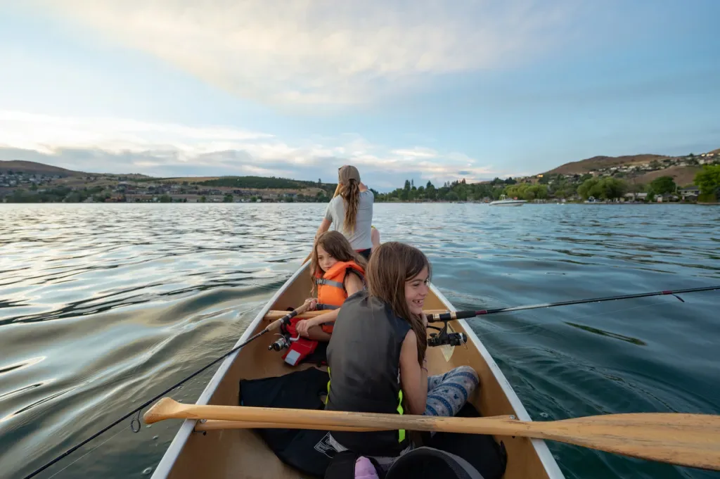 A woman paddles a boat while two young girls fish at a place similar to Lake Catherine