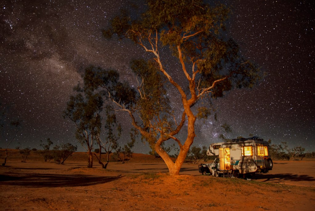 An RV parked beside a beautiful tree under millions of stars