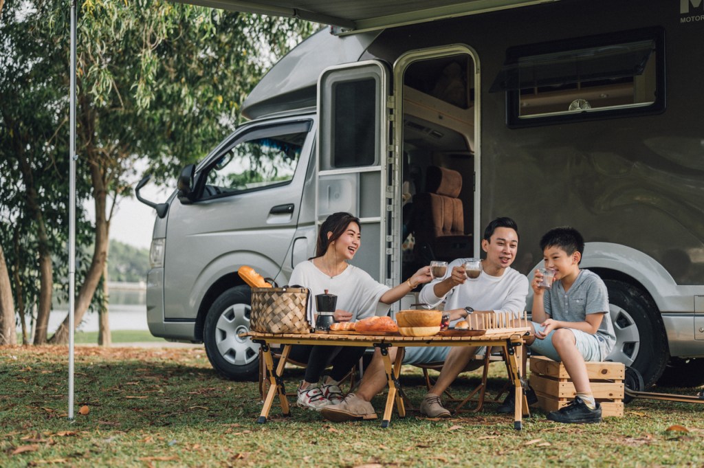 A happy family sitting outside their campervan at a campground