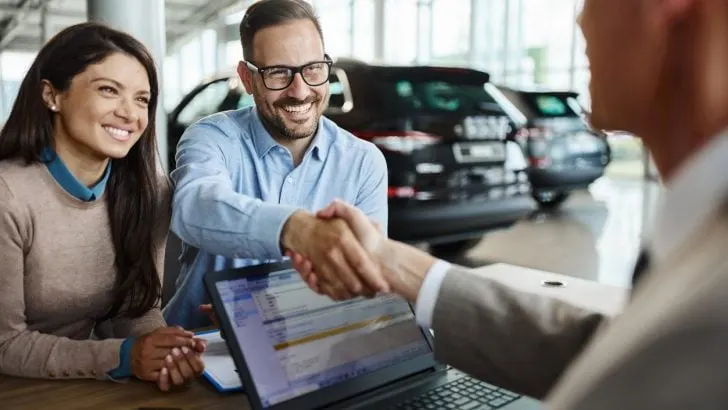Young couple shaking hands with a car salesman
