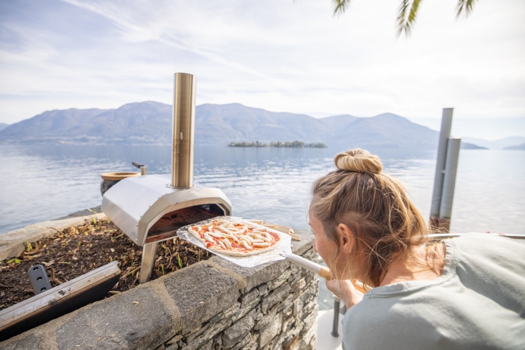 A woman placing a pizza into a portable pizza oven