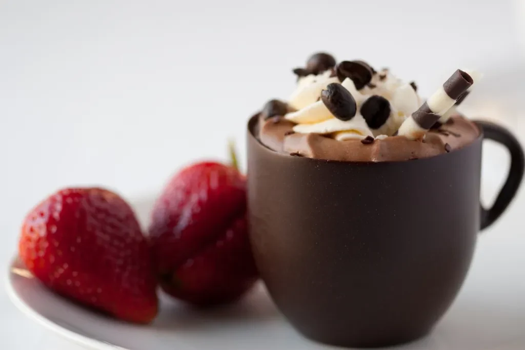 Chocolate cup filled with chocolate mousse topped with whipped cream.  Strawberries on the side. A possible offering at a chocolate festival.