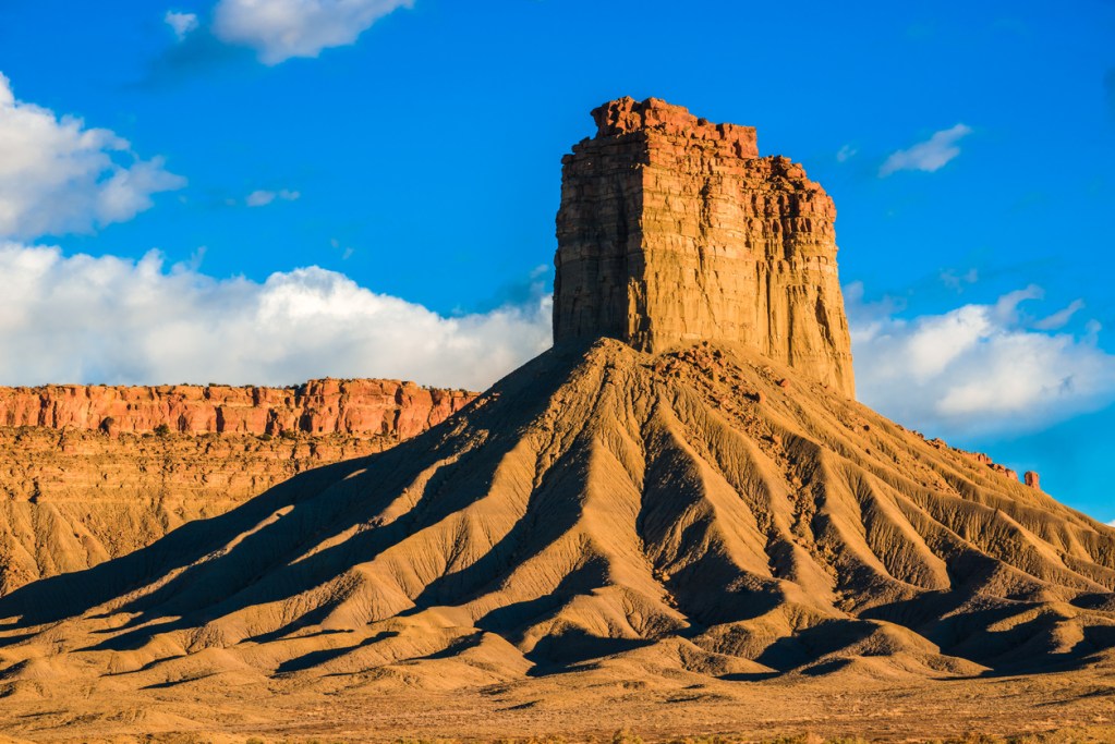 The dramatic lumionus orange and brilliant blue colors of Chimney Rock butte and bluff rock formation during the golden hour just before sunset. On highway 491 near Cortez Colorado.