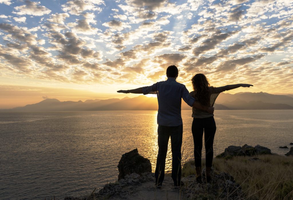 Portrait of couple standing with arms outstretched on cliff at sunset that could be Mortons on the Move