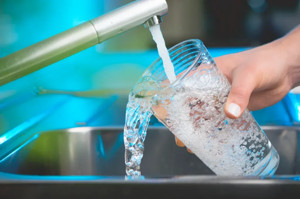 Woman filling a glass of water at a kitchen faucet, perhaps from the RV freshwater tank
